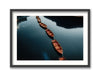 A framed artwork featuring a photograph of wooden boats on water with a backdrop of lush greenery and mountains.