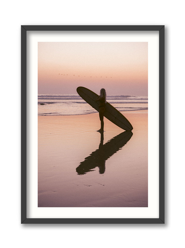 Framed artwork of a person holding a surfboard on a beach at sunset.