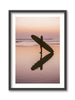 Framed artwork of a person holding a surfboard on a beach at sunset.