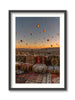 A framed artwork depicting hot air balloons floating over a landscape with ancient cave dwellings and fairy chimneys during sunrise. Cappadocia